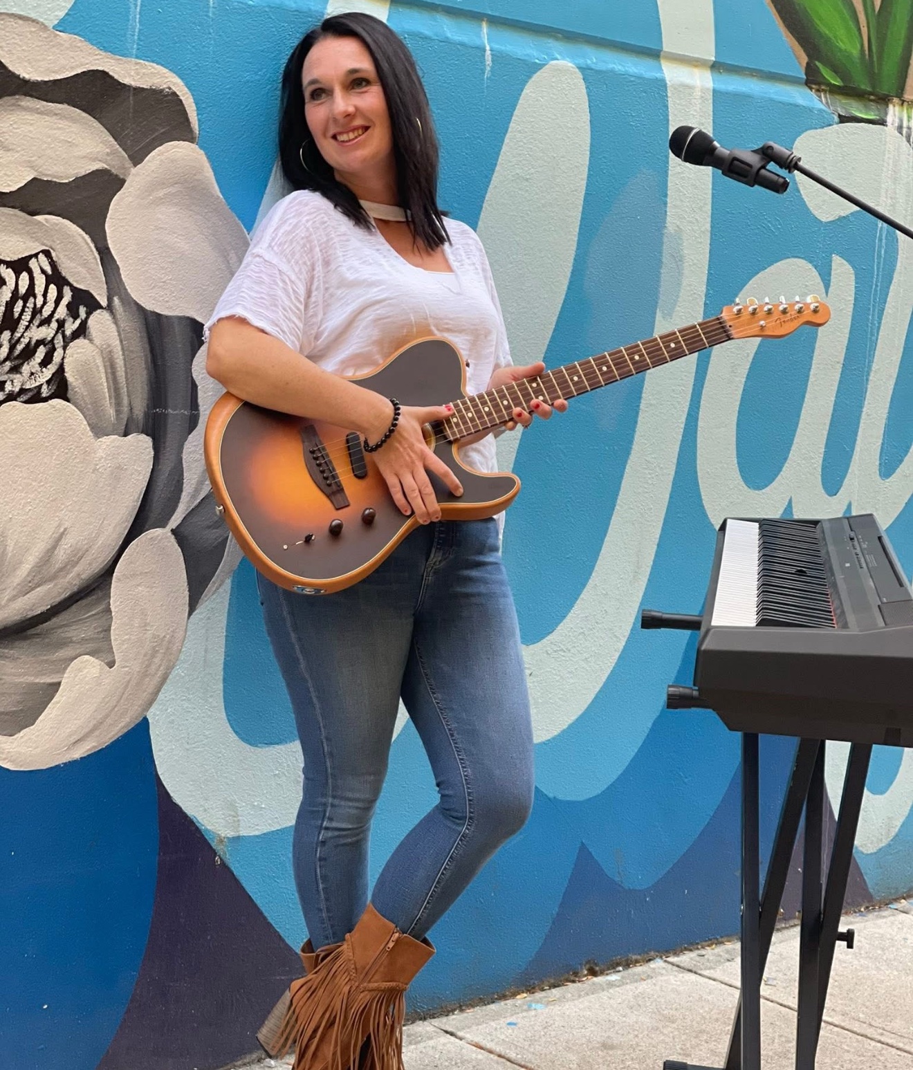 Angie Marquardt playing electric guitar in front of a colorful mural