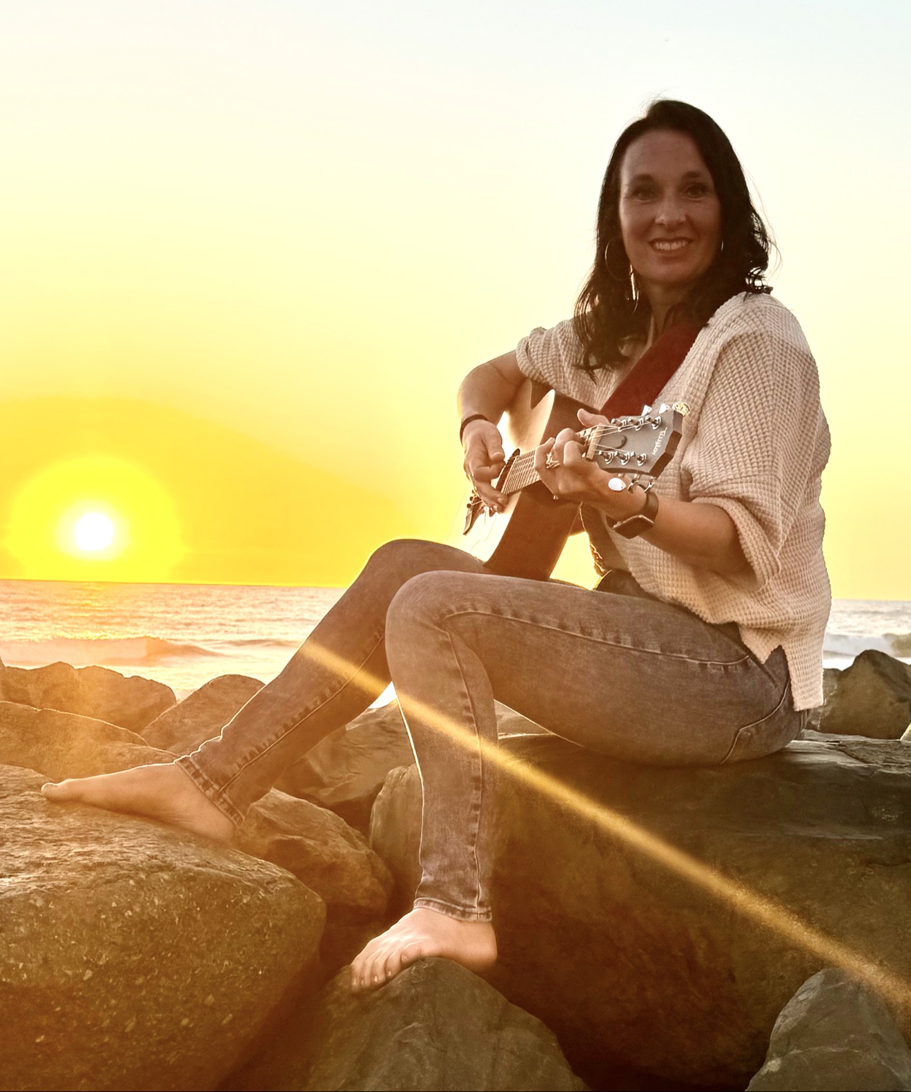 Angie Marquardt playing guitar at sunset by the water